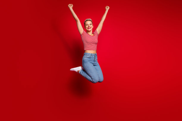 穿着时尚衣服的兴奋女孩在红色背景上跳起庆祝成功的全身照片图片下载