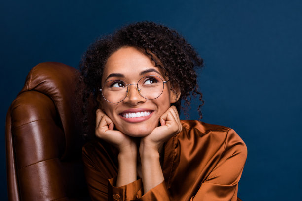 漂亮年轻女孩的照片肖像，坐在可爱的老板椅上，穿着时尚的棕色丝绸正装，背景为深蓝色。图片下载