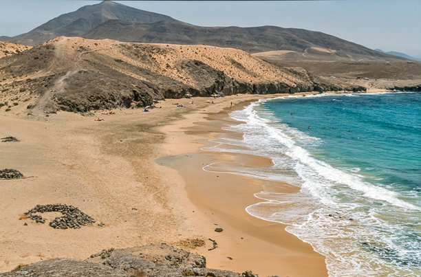 扫描的历史彩色照片，展示了加那利岛兰萨罗特的“Congrio海滩”及其背景中的“哈查格兰德”山，拍摄于夏季。图片下载