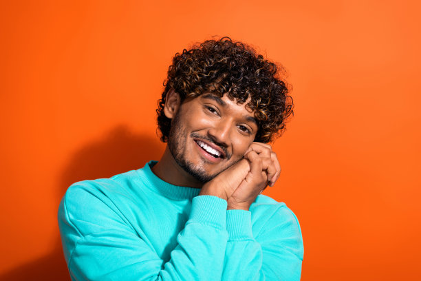 微笑的可爱男朋友与女友手牵手，欣赏她穿着明亮毛衣的照片肖像，背景为橙色。图片下载