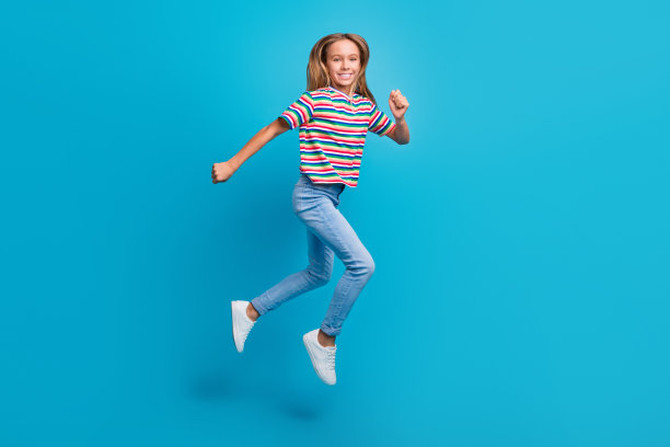 充满乐观情绪的少女穿着彩色T恤和牛仔裤，在蓝色背景下奔跑购物的全身照片图片下载