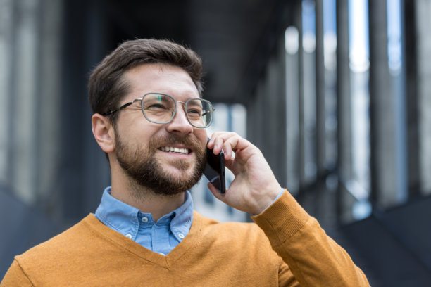 一位帅气的男人在街上微笑着打电话的特写照片图片下载