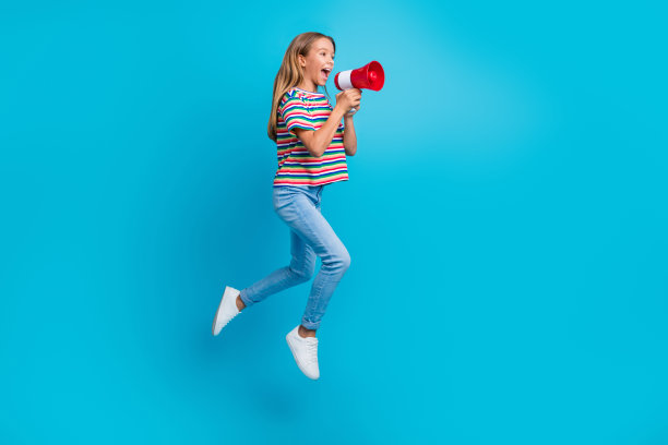 穿着条纹T恤的活泼女学生在空旷的蓝色背景上跳跃，宣布促销活动的全身照片图片下载