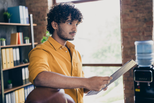 穿着黄色衬衫的迷人年轻男子在现代家居设计的办公室里手持文件进行会议演示策略的照片肖像图片下载