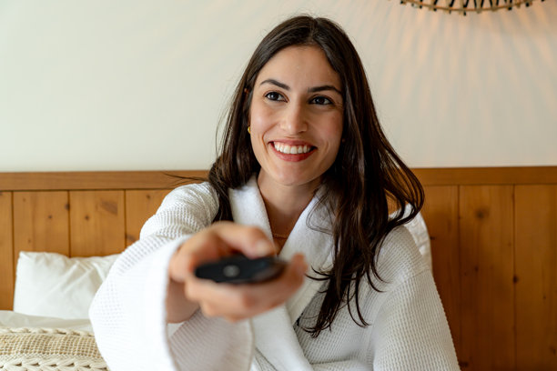 微笑的女性在酒店房间里使用遥控器，享受电视节目图片下载
