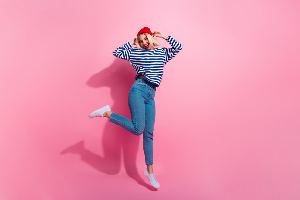 可爱的快乐女孩穿着条纹衬衫在粉色背景上高高跳起，尽情玩乐的全身照片图片下载