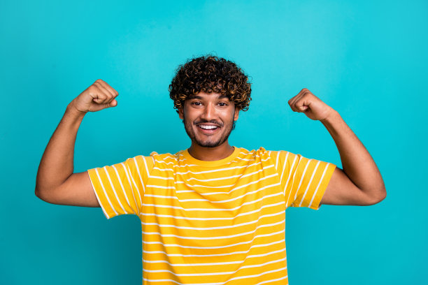 年轻男性的照片肖像，双拳举起，肌肉强壮，穿着时尚的条纹黄色服装，背景为青色。图片下载