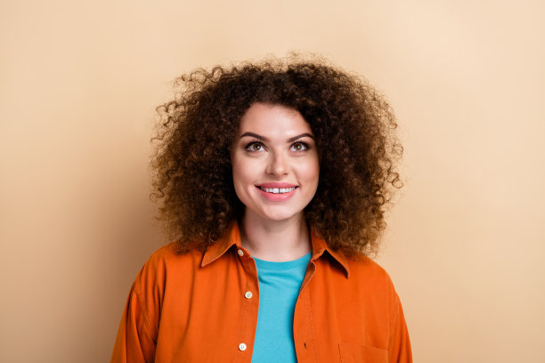 漂亮年轻女孩的照片肖像，穿着时尚的橙色服装，仰望空旷的空间，背景为米色。图片下载