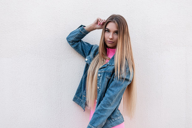 身穿时尚蓝色牛仔夹克的美丽年轻女性，拥有奢华的金色长发，在城市的复古建筑旁摆姿势。漂亮的女孩在夏日的户外放松。复古风格。图片下载