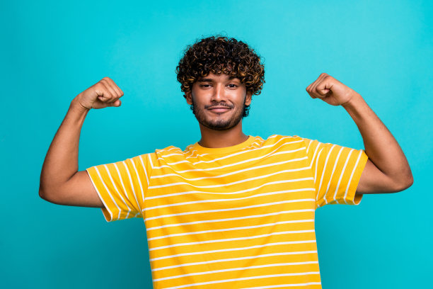 吸引人的年轻男子的照片肖像，展现力量的拳头，穿着时尚的条纹黄色衣服，背景为水绿色。图片下载