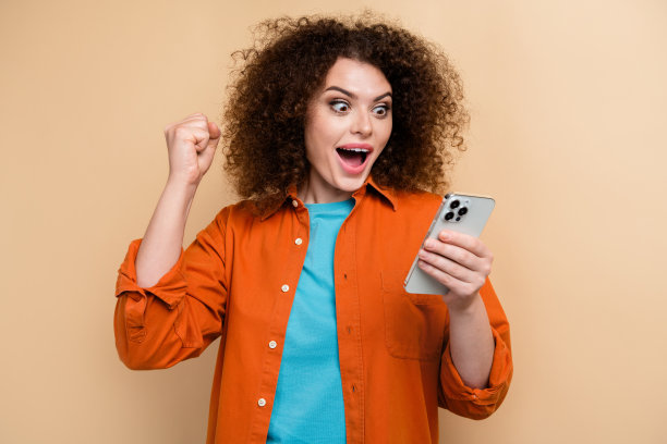 年轻女孩的照片肖像，兴奋地举起拳头庆祝中奖，穿着时尚的橙色服装，背景为米色。图片下载