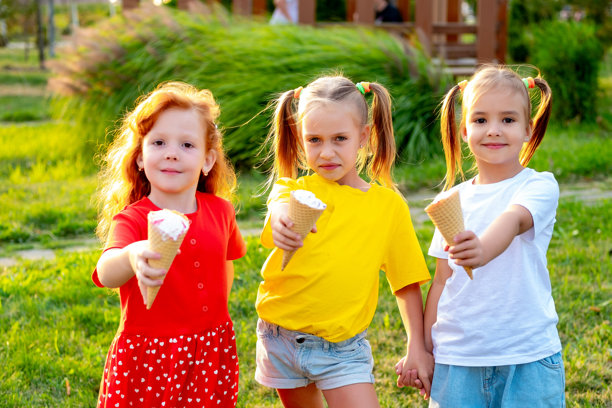 快乐的孩子们在公园的绿草坪上吃冰淇淋，明亮的夏季儿童假日照片，三个小女孩在夏天欢笑玩耍。图片下载