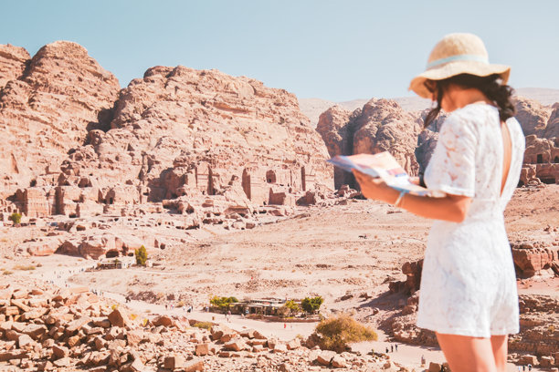 时尚的白人女性游客，阅读地图，计划探索约旦古老而迷人的佩特拉城市的景点。色彩丰富的照片。休闲、度假和旅行的概念。图片下载