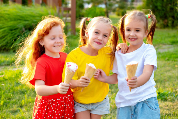 快乐的孩子们在公园的绿草坪上吃冰淇淋，明亮的夏季儿童假日照片，三个小女孩在夏天欢笑玩耍。图片下载