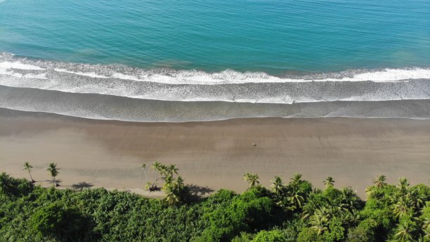 哥斯达黎加乌维塔海滩的无人机航拍照片，蓝色海洋、小波浪和深绿色的棕榈树。浅水中云朵的理想倒影与深绿色热带丛林相映成趣。冒险与独自背包旅行到中美洲。图片下载