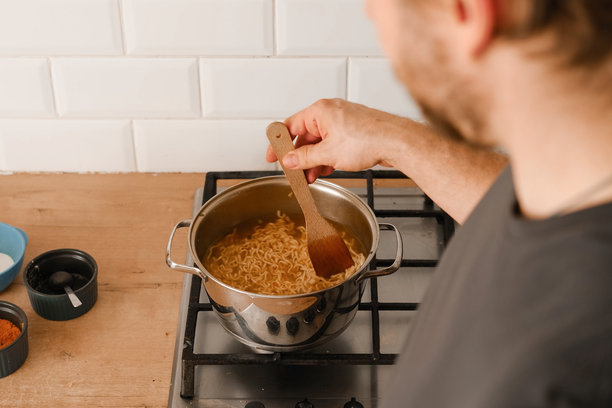男子在家厨房的炉子上煮拉面。传统亚洲美食。特写照片展示男子的手在盛放配有新鲜蔬菜的意大利面。准备自制菜肴。图片下载
