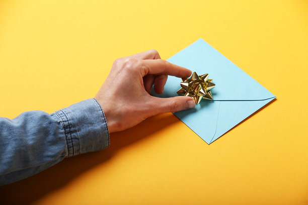 一张第一人称视角的照片，手握着蓝色信封和白色卡片，背景为孤立的黄色，留有空白空间。图片下载