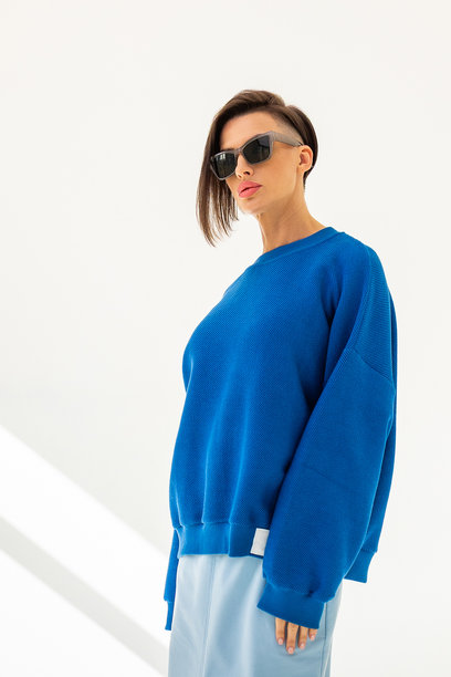 穿着蓝色卫衣和浅蓝色裙子的优雅女性，背景为白色。时尚女性风格。摄影棚拍摄。竖版照片。图片下载