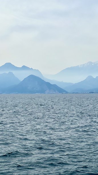 山脉轮廓在平静海面上方，水面闪烁着光芒的竖版照片图片下载