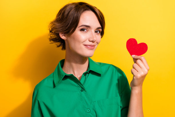 穿着绿色衬衫、可爱甜美的小女孩在黄色背景下展示小红心的照片图片下载