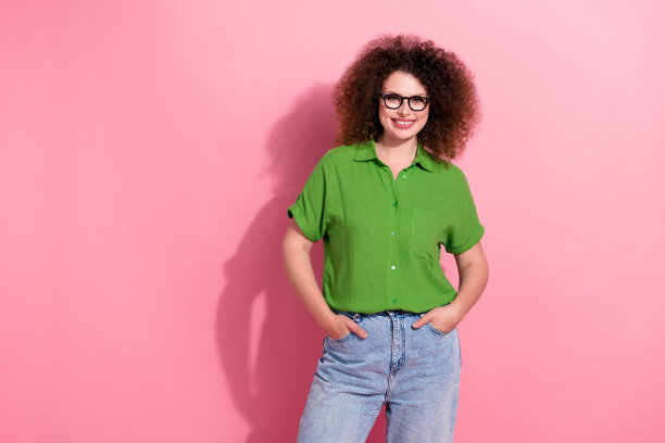 年轻女士的照片肖像，双手插口袋，穿着时尚的绿色服装，背景为粉色。图片下载