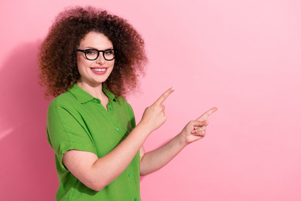 穿着时尚绿色衣服的迷人年轻女性在粉色背景前指向空白处的照片肖像图片下载