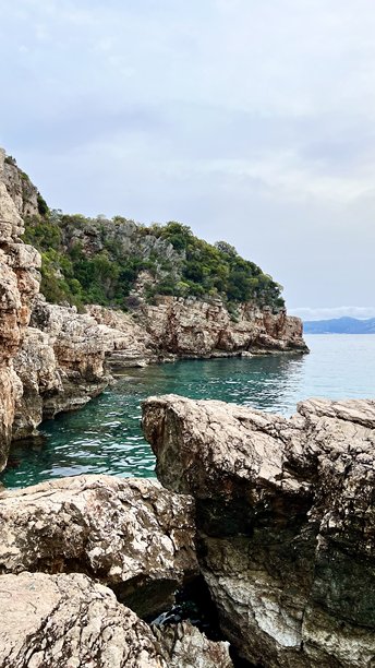 陡峭的橙色和白色岩石悬崖高耸于宁静的碧绿色水面之上，竖版照片。图片下载