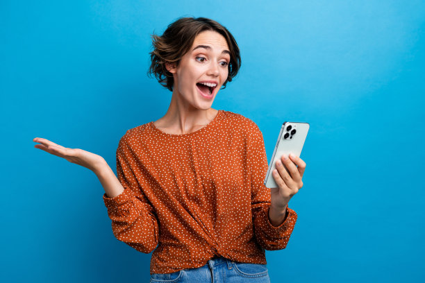 吸引人的年轻女性在蓝色背景下穿着时尚的棕色衣服，兴奋地进行在线视频通话的照片肖像图片下载