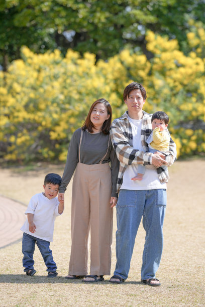 在日本的一个阳光明媚的森林公园里，一对日本夫妇和他们3岁的儿子以及6个月大的宝宝站在一片黄色花海旁。这张照片捕捉了一个安静而温馨的家庭时刻。图片下载