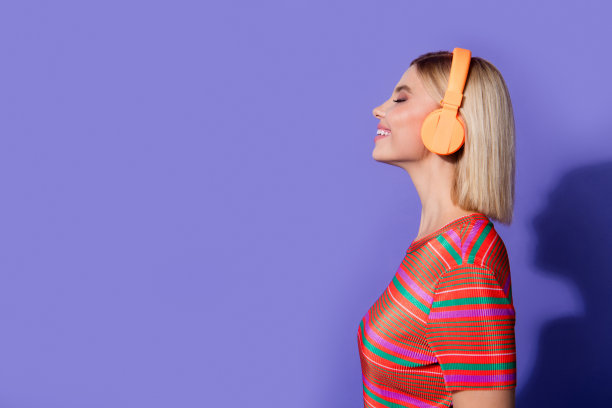 侧面视角照片，展示穿着条纹T恤的无忧无虑的女友，耳朵里戴着耳机，背景为紫色。图片下载