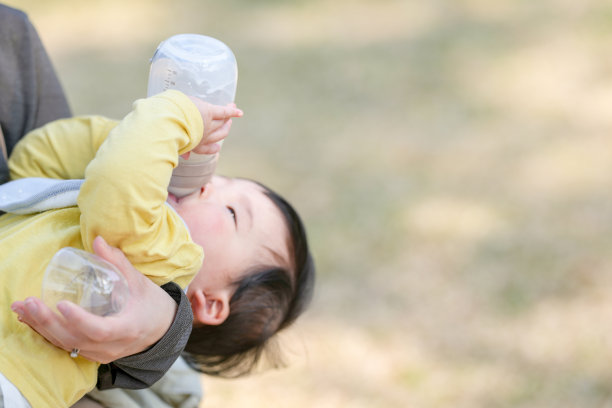 在日本的一个阳光明媚的森林公园里，一位三十多岁的日本妈妈坐在长椅上，正在给她六个月大的宝宝喂奶。这张照片捕捉了一个安静而温馨的户外家庭时刻。图片下载