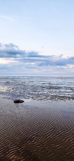 春季风景。美丽的海湾晨曦全景。明亮的光线下，水面上漂浮着积云。海岸线上有冰雪和岩石。阳光的光芒在海面上反射。竖版照片图片下载