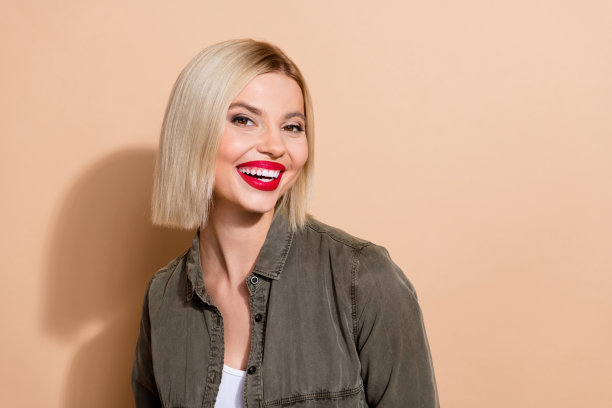 特写照片，漂亮的金发女士露出洁白的牙齿微笑，涂着红色唇膏，妆容明亮，背景为米色。图片下载