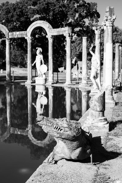 黑白照片展示了古罗马柱廊和装饰人工池塘边缘的雕塑，位于意大利花园中。图片下载