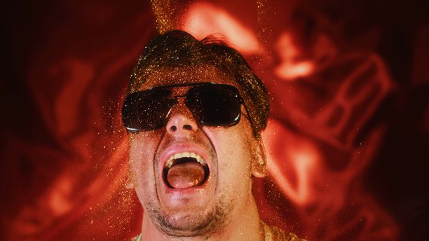 疯狂有趣的男人用闪光颗粒洒自己。搞笑的照片，搞怪的表情，吐着舌头。滑稽的搞笑肖像，戴着太阳镜的家伙在脸上和嘴里洒金色闪粉，展现出最佳的搞笑表演。图片下载