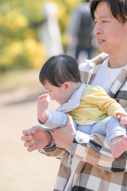 在日本的一个阳光明媚的森林公园里，一对日本夫妇和他们3岁的儿子以及6个月大的宝宝站在一片黄色花海旁。这张照片捕捉了一个安静而温馨的家庭时刻。图片下载