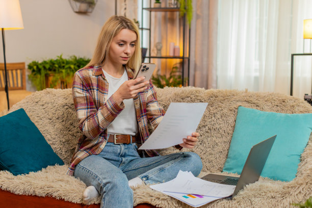 成年女性在家用智能手机拍摄文件照片，为远程工作做准备，旁边有笔记本电脑。图片下载
