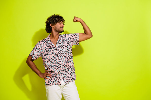 穿着时尚粉色豹纹衣服的迷人年轻男子在黄色背景下展示肌肉的照片肖像图片下载