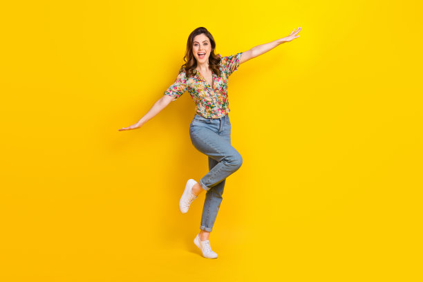 兴奋可爱的女士穿着复古花卉印花衬衫，双臂自然垂放，在黄色背景下尽情享受乐趣的全身照片。图片下载