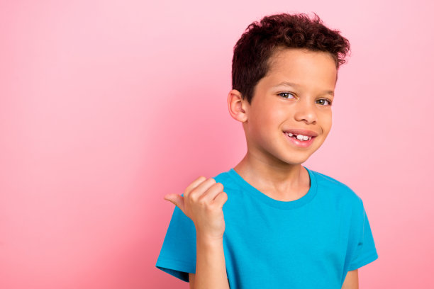 时尚穿着蓝色衣服的小男孩在粉色背景前指向空白处的照片肖像图片下载