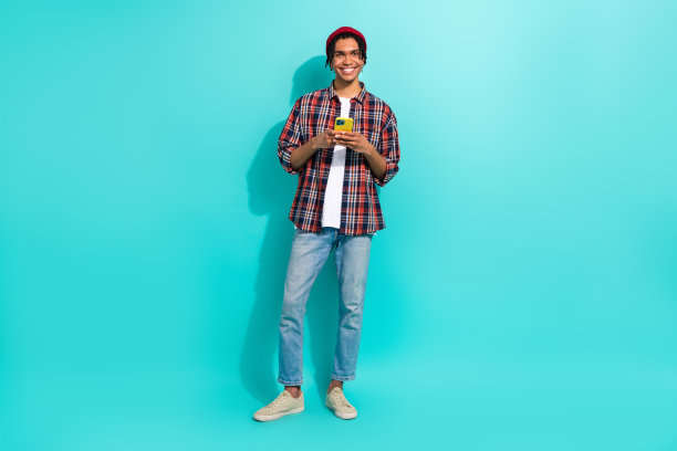 全身照片，积极向上的年轻男子手持智能手机，正在打字撰写博客，背景为水绿色。图片下载