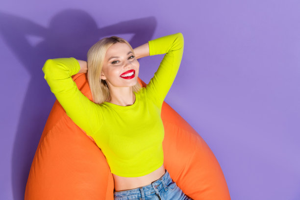 高角度拍摄的照片，展现了一位穿着时尚绿色青柠色服装的快乐美丽女孩，舒适地躺在空旷的包上，背景为紫色。图片下载