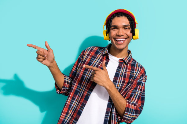 帅气年轻男子的照片肖像，手指指向空白处，穿着时尚的格子服装，背景为水绿色。图片下载