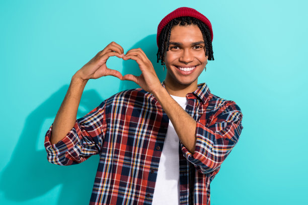 帅气年轻男子的照片肖像，手指比出心形，穿着时尚的格子服装，背景为水绿色。图片下载