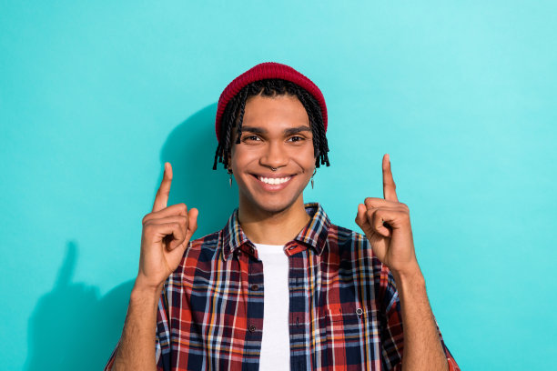 吸引人的年轻男士的照片肖像，手指指向空白处，穿着时尚的格子服装，背景为青色。图片下载