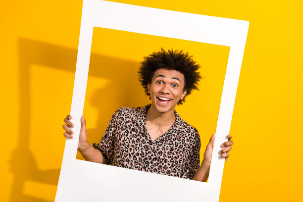 穿着豹纹衬衫的兴奋快乐男孩在黄色背景下拿着照片纸和相框图片下载