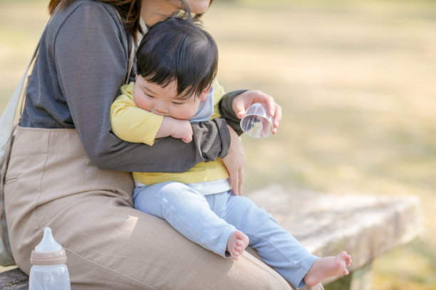 在日本的一个阳光明媚的森林公园里，一位三十多岁的日本妈妈坐在长椅上，抱着她六个月大的宝宝。这张照片捕捉了春天温暖中一个安静而温馨的家庭时刻。图片下载