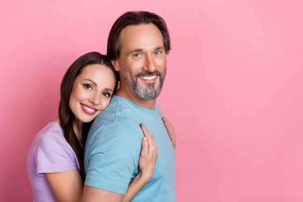 迷人的情侣侧面照片，妻子在粉色背景下从后面支持丈夫，彼此拥抱。图片下载