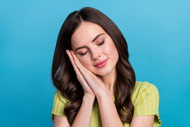 穿着绿色T恤的年轻棕发女士在蓝色背景上休息和睡觉的照片图片下载