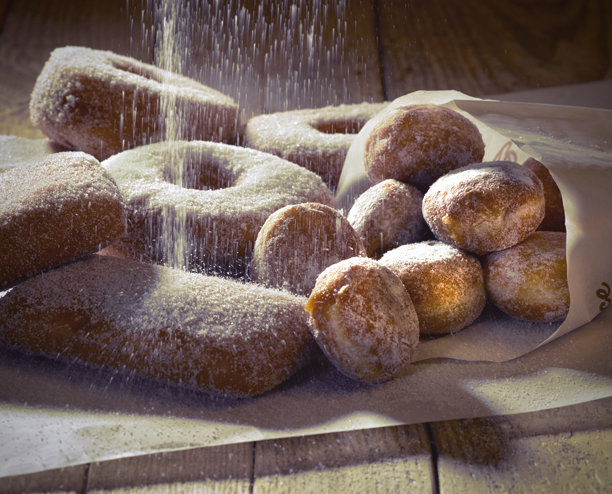 新鲜糖霜甜甜圈的工作室照片。糖从上方洒落。木质背景和工作室中的聚光灯。图片下载